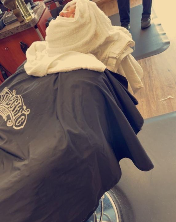 man with hot towel on face in barbers chair
